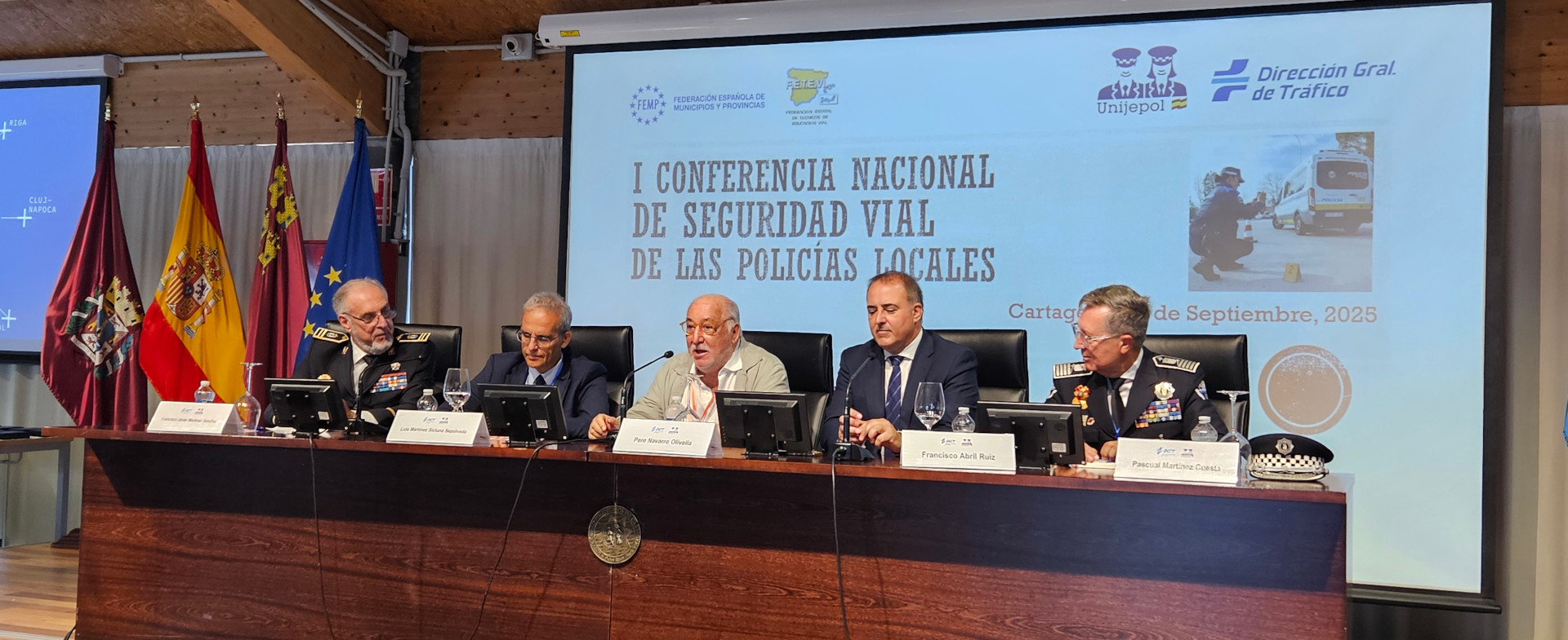 Mesa inaugural de la I Conferencia Nacional de Seguridad Vial de las Policías Locales en Cartagena, con cinco ponentes uniformados y autoridades sentados frente a un cartel proyectado con el título del evento Mesa inaugural de la I Conferencia Nacional de Seguridad Vial de las Policías Locales en Cartagena, con cinco ponentes uniformados y autoridades sentados frente a un cartel proyectado con el título del evento