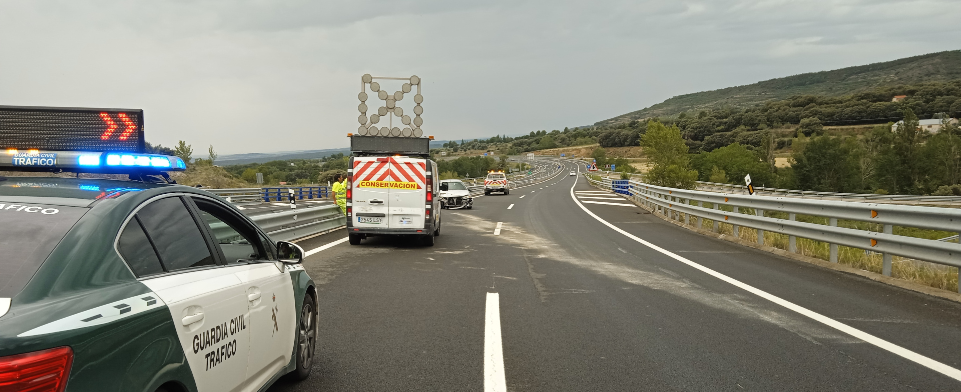 Carretera con curvas. A la izquierda, un coche de la Guardia Civil de Tráfico detenido. Al fondo, una furgoneta de Conservación de Carreteras está situada frente a un coche accidentado Carretera con curvas. A la izquierda, un coche de la Guardia Civil de Tráfico detenido. Al fondo, una furgoneta de Conservación de Carreteras está situada frente a un coche accidentado