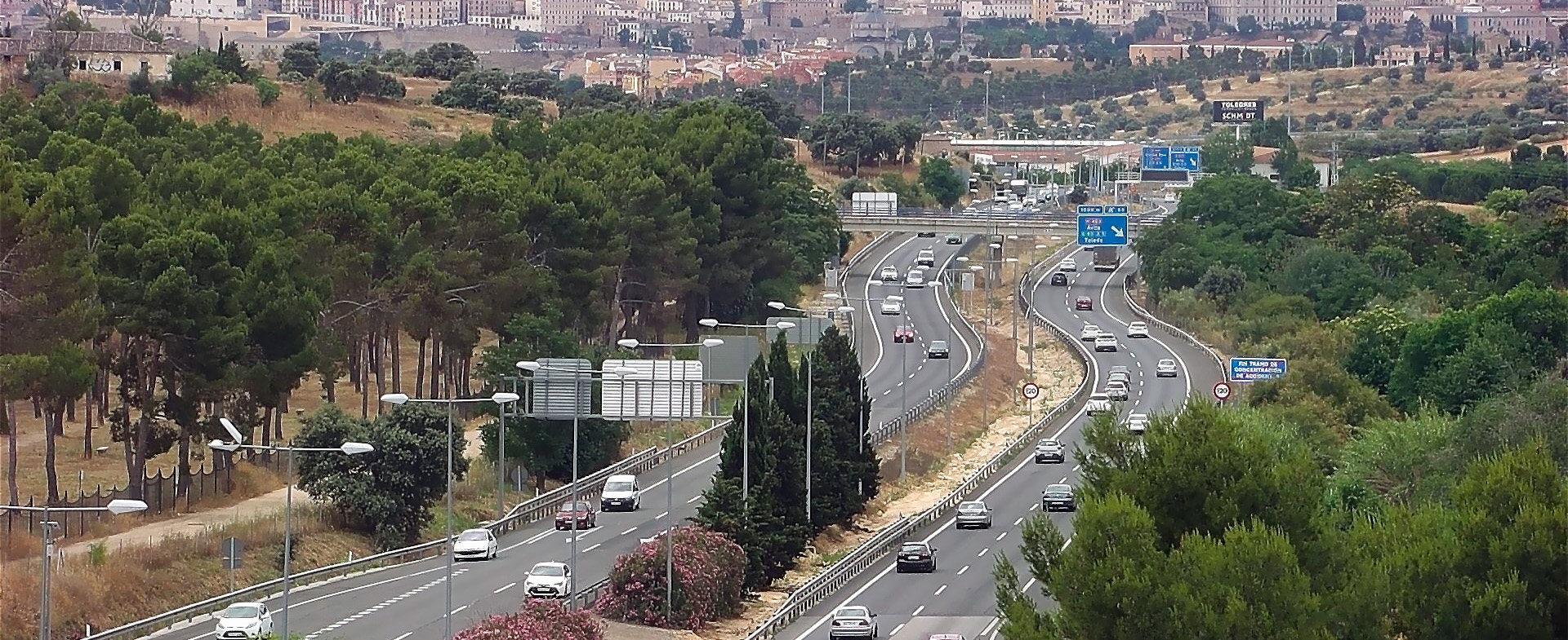 Vista aérea de una carretera de acceso a una ciudad con dos carriles por sentido, tráfico denso de vehículos y árboles alineados a los lados Vista aérea de una carretera de acceso a una ciudad con dos carriles por sentido, tráfico denso de vehículos y árboles alineados a los lados
