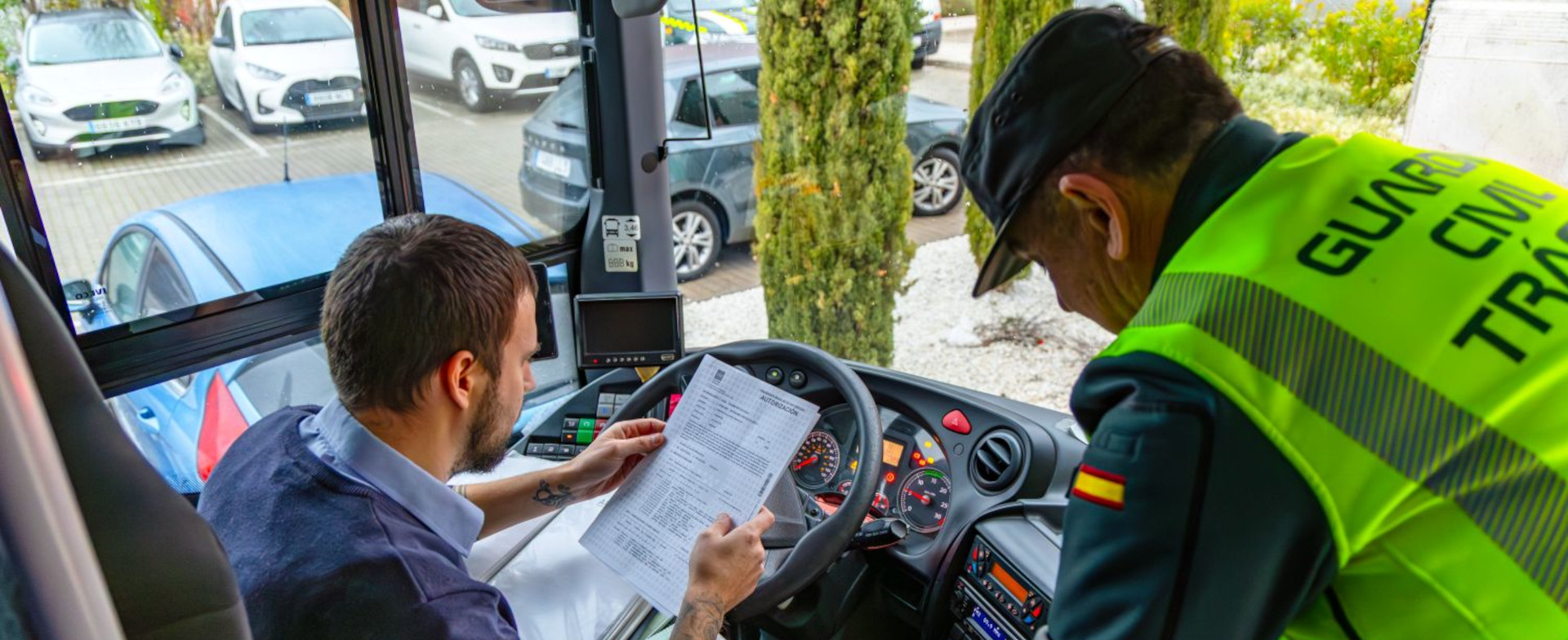 Un conductor de autobús sentado en el asiento del conductor con un papel entre sus manos y un guardia civil de pie a su lado en el interior de un autobús Un conductor de autobús sentado en el asiento del conductor con un papel entre sus manos y un guardia civil de pie a su lado en el interior de un autobús
