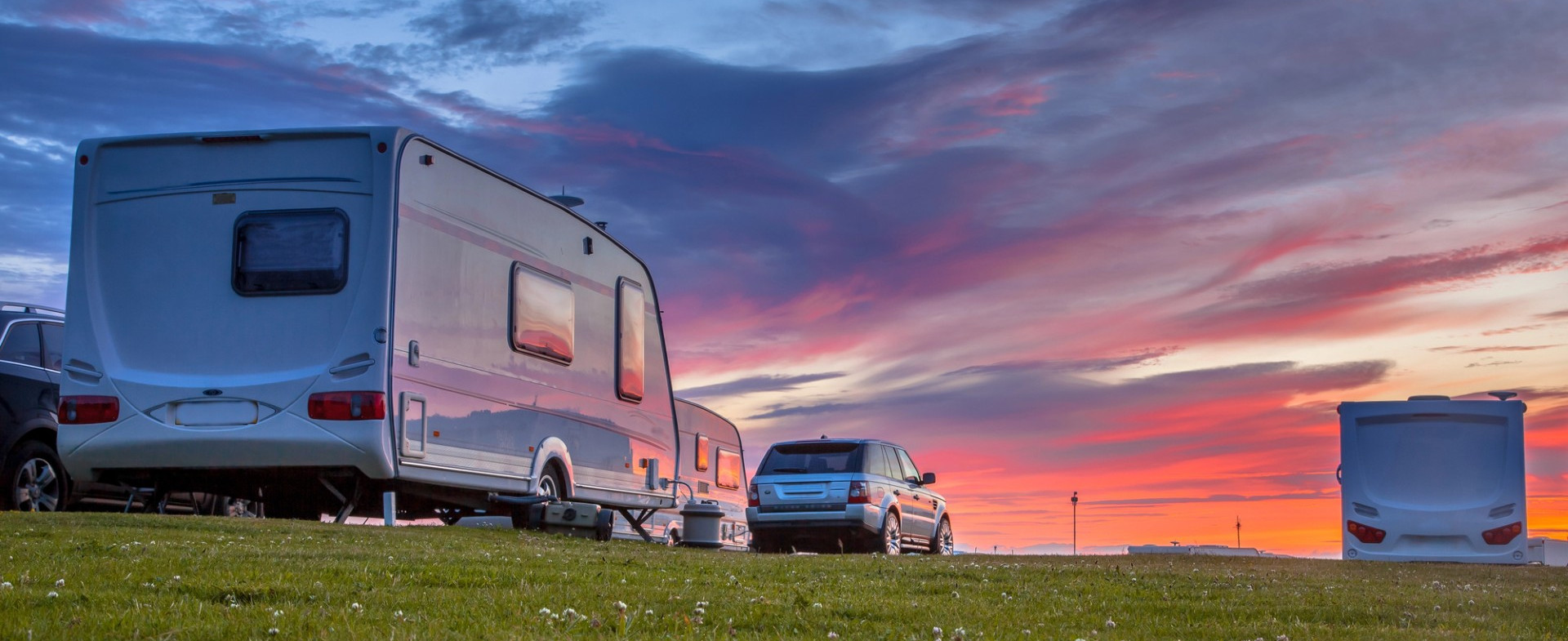 Imagen tres autocaravanas y un coche aparcados en un campo al atardecer.