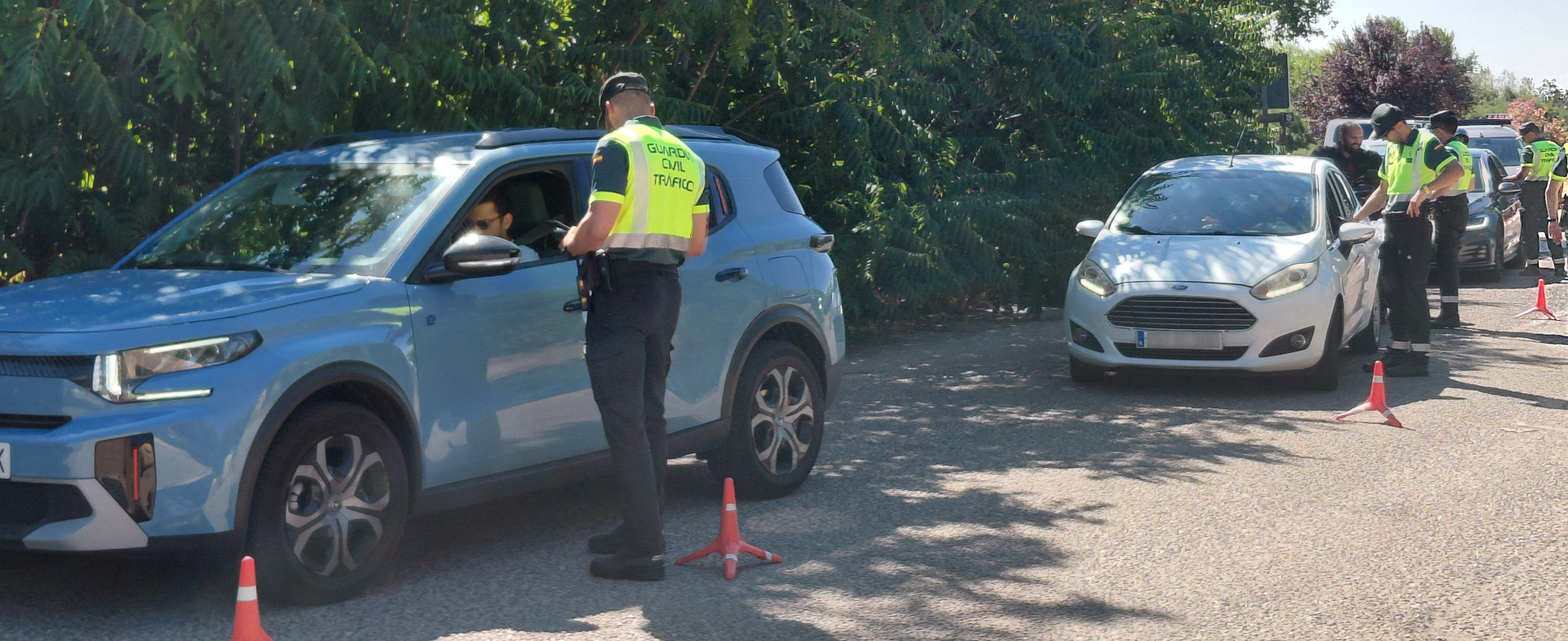 Un grupo de guardias civiles realiza un control de alcohol y drogas a los conductores de varios coches detenidos en una carretera, junto a una arboleda